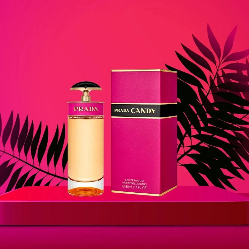 Prada Candy perfume bottle and packaging on a pink background with black leaves.