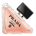 A triangular glass bottle of Prada Paradoxe eau de parfum with a black cap, showcasing the pinkish-tinted liquid inside.
