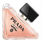 A triangular glass bottle of Prada Paradoxe eau de parfum with a black cap, showcasing the pinkish-tinted liquid inside.