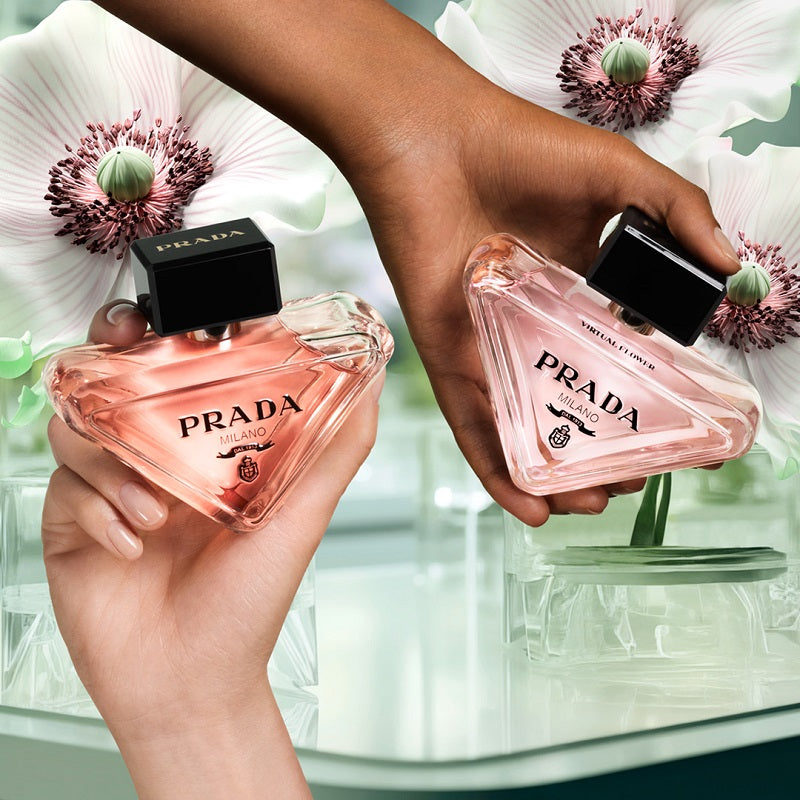 Two hands holding Prada perfume bottles against a floral background
