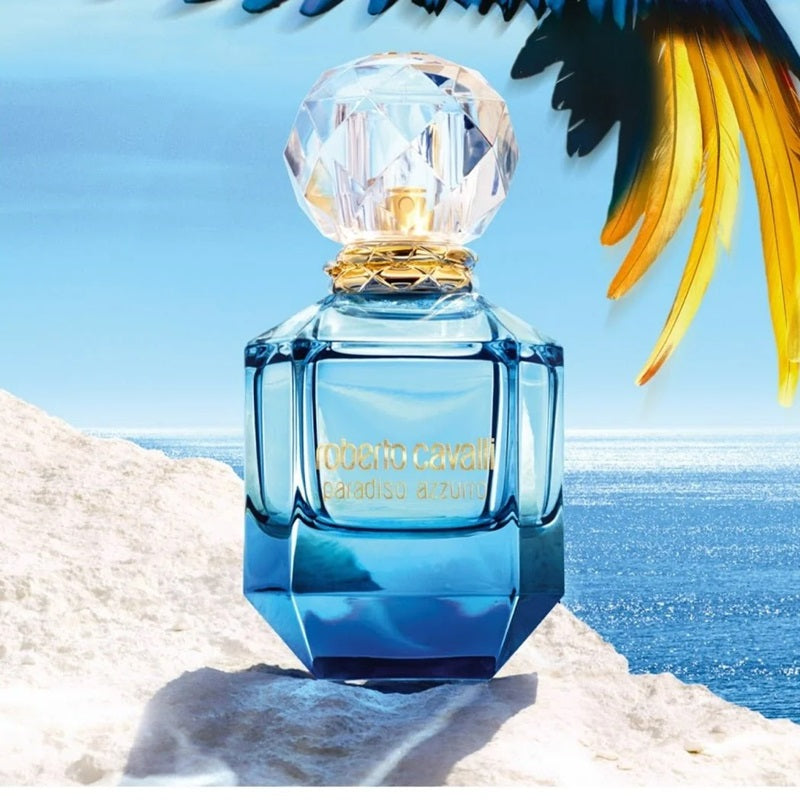 Blue Roberto Cavalli perfume bottle on a beach with ocean and palm tree in the background