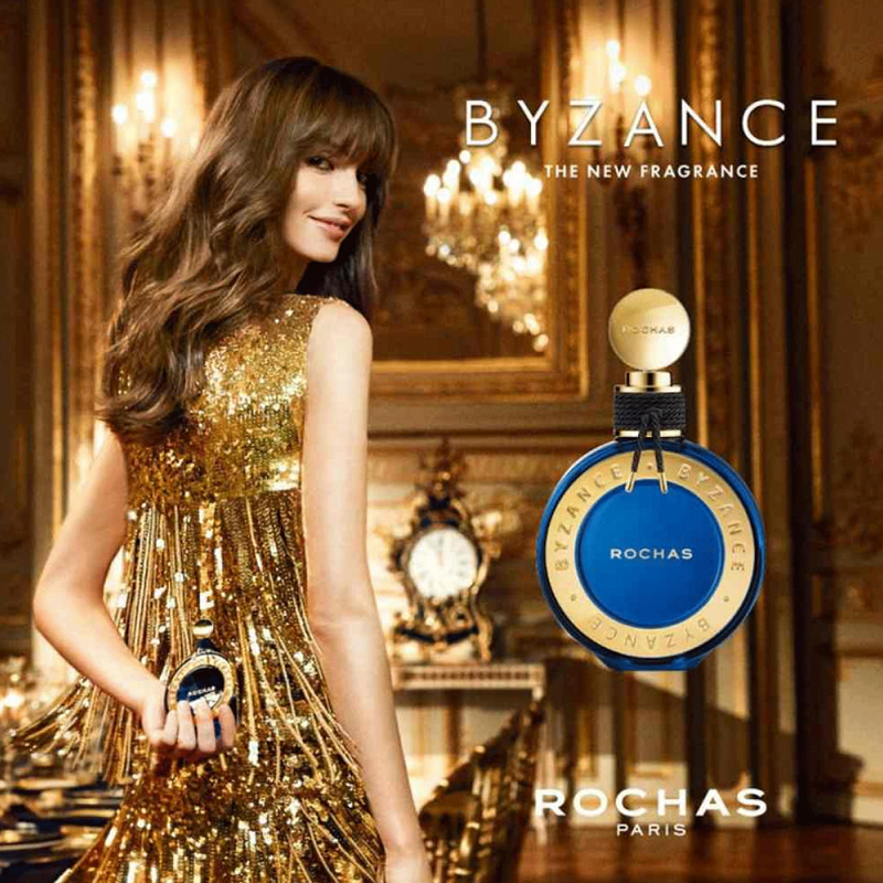 A woman in a gold sequined dress stands in an ornate room while holding a small blue and gold perfume bottle. Large text reads 'BYZANCE THE NEW FRAGRANCE' and 'ROCHAS PARIS' appears at the bottom right.
