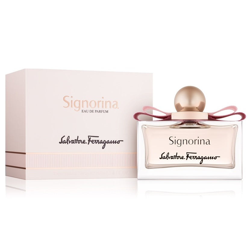 A product image featuring the Signorina Eau de Parfum by Salvatore Ferragamo, with the perfume bottle displayed in front of its packaging box. The bottle is clear with a gold cap, and the label has the name 'Signorina' on it.