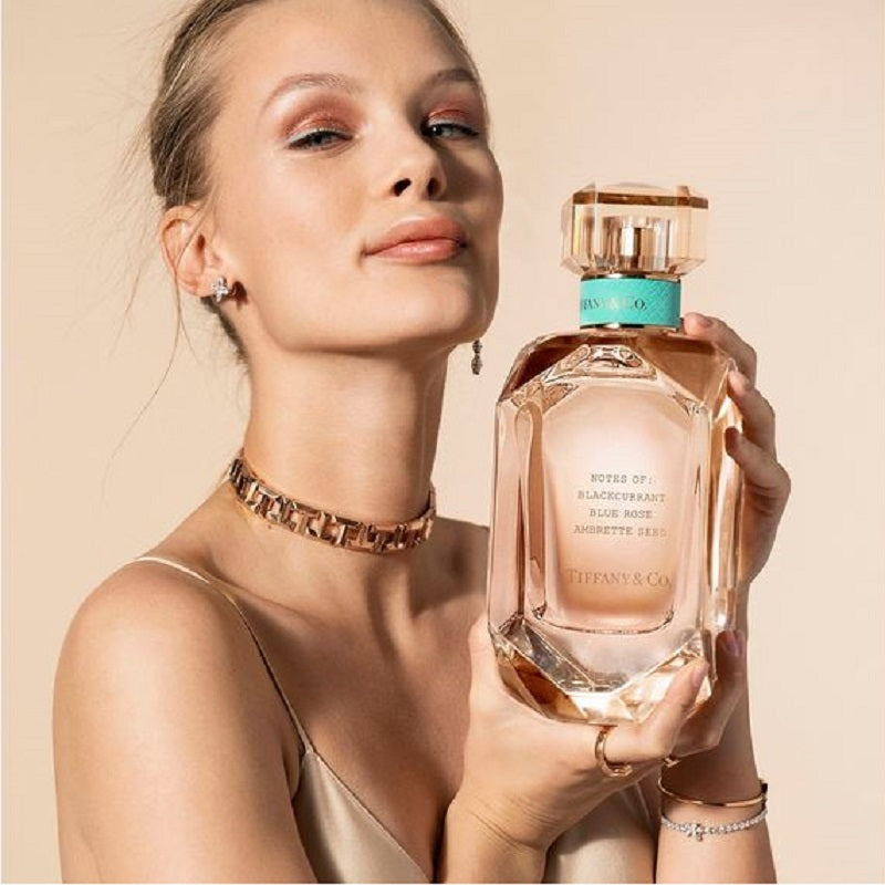 Model holding a Tiffany Rose Gold Eau de Parfum by Tiffany & Co. styled among soft pink florals and rose gold accents reflecting elegance, joy and modern femininity.