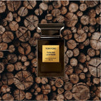Tom Ford Tuscan Leather perfume bottle on a background of stacked wooden logs