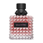 A glass bottle of Valentino Donna Born In Roma perfume with a black cap and a pink-hued body featuring a geometric pattern.