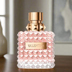 Valentino perfume bottle with pink diamond pattern and gold cap on a wooden surface.