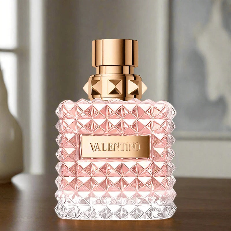 Valentino perfume bottle with pink diamond pattern and gold cap on a wooden surface.