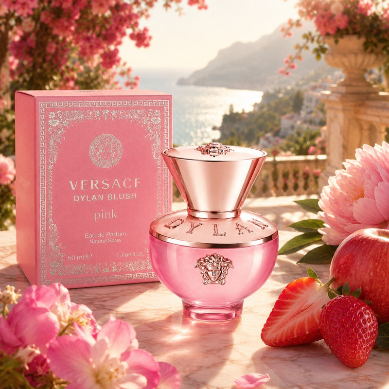 Versace Dylan Blush pink Eau de Parfum bottle and its pink packaging box, styled on a marble surface with pink flowers, strawberries, and a scenic coastal background.