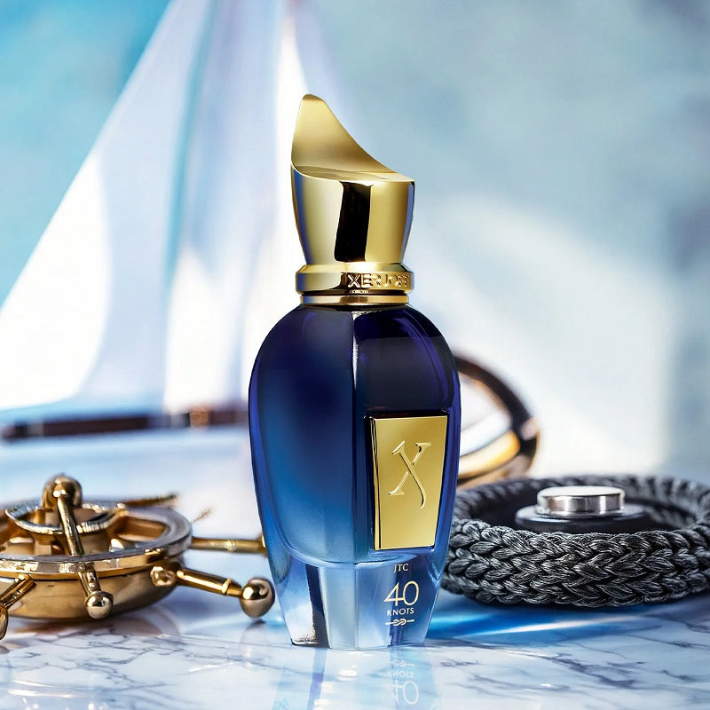 Blue perfume bottle with gold cap and label on a marble surface with nautical-themed decor.