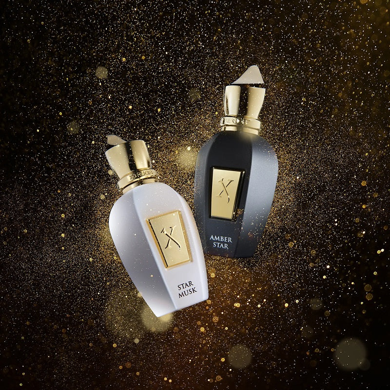 Two perfume bottles, one white and one black with gold accents, on a dark background.