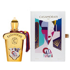 The image shows a Casamorati Casafutura Eau De Parfum bottle with a gold and clear design, accompanied by a card with a colorful abstract face illustration.