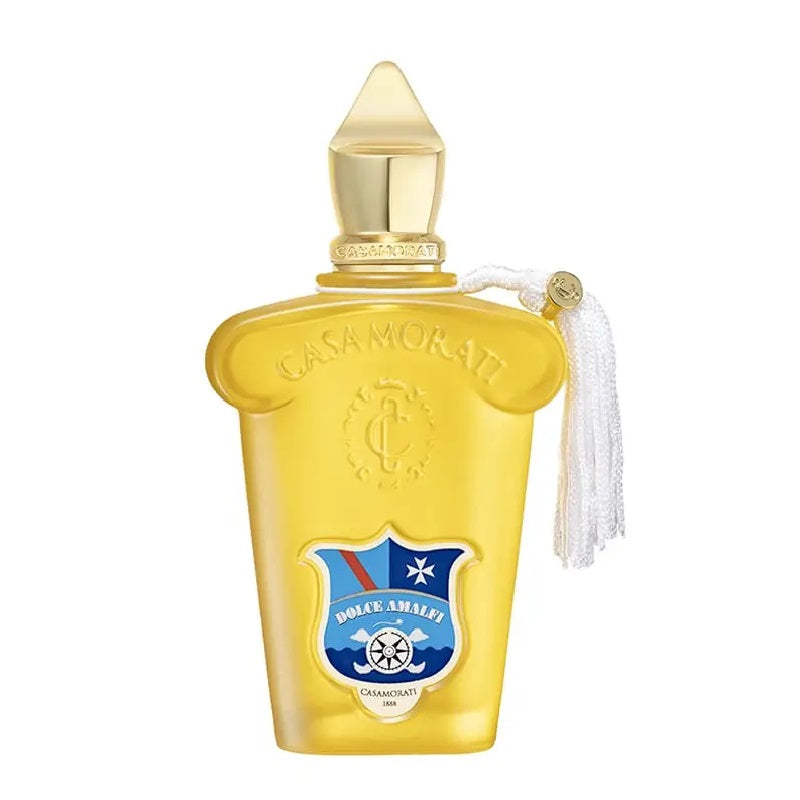 A yellow glass bottle of Casamorati Dolce Amalfi Eau de Parfum by Xerde, with a label featuring a blue and white crest and a white tassel on the cap.