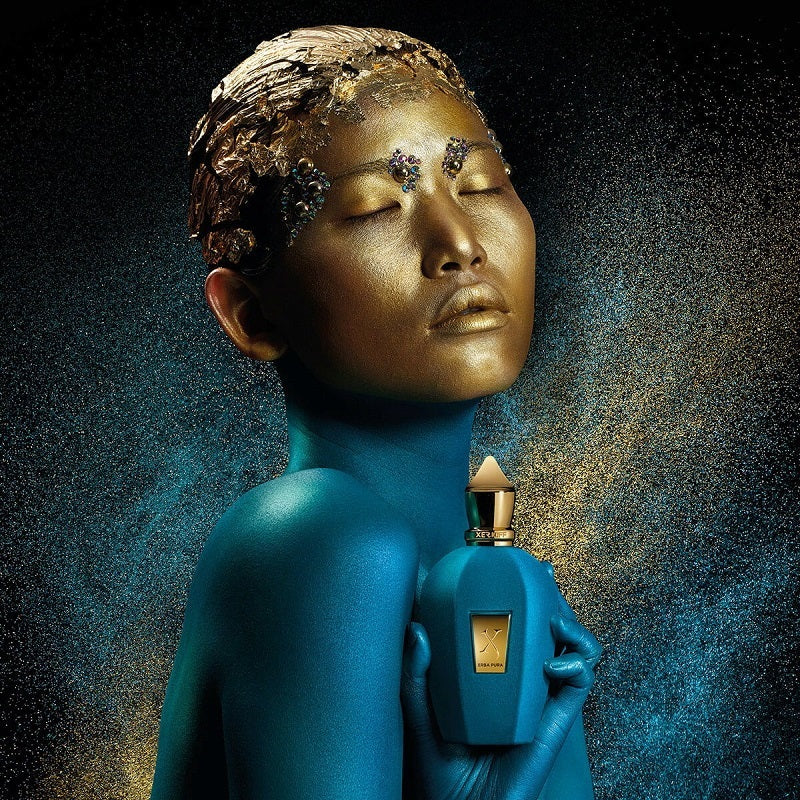 Blue-skinned figure holding a gold and blue perfume bottle against a dark background