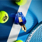 Blue perfume bottle with gold cap on a tennis court surface with tennis balls.