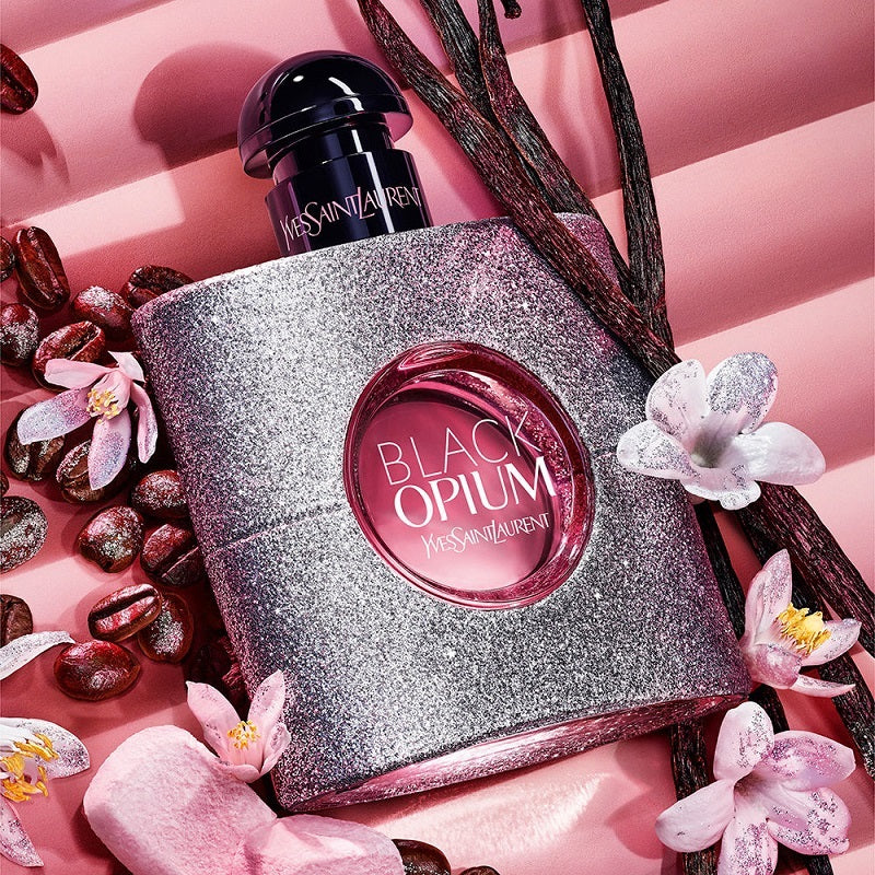 Yves Saint Laurent Black Opium perfume bottle with flowers and beans on a pink background