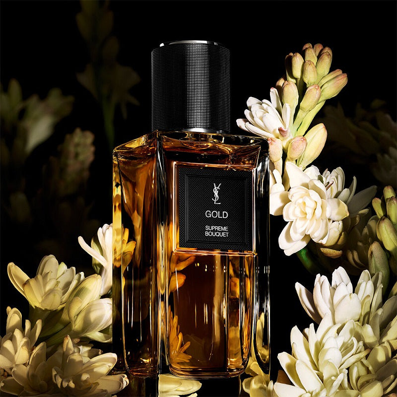 Perfume bottle labeled 'Gold' surrounded by flowers on a dark background