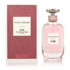 A bottle of Coach Dreams Eau de Parfum next to its pink box, with the brand name and product name displayed.