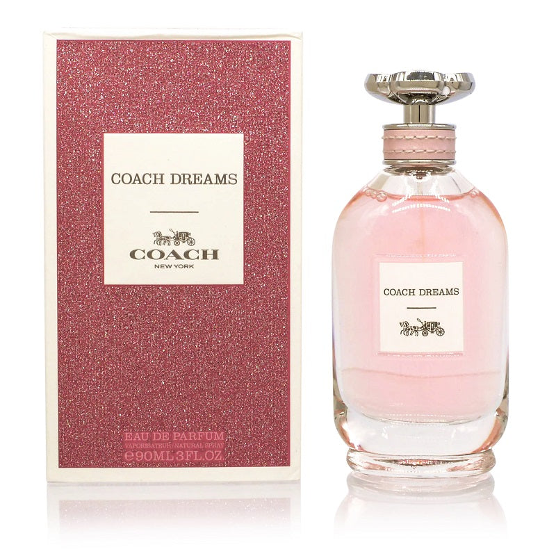 A bottle of Coach Dreams Eau de Parfum next to its pink box, with the brand name and product name displayed.