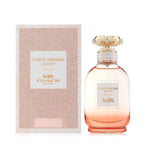 A bottle of Coach Dreams Sunset Eau de Parfum by Coach, with a pink hue and a gold cap, alongside its packaging.