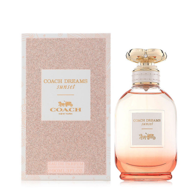 A bottle of Coach Dreams Sunset Eau de Parfum by Coach, with a pink hue and a gold cap, alongside its packaging.