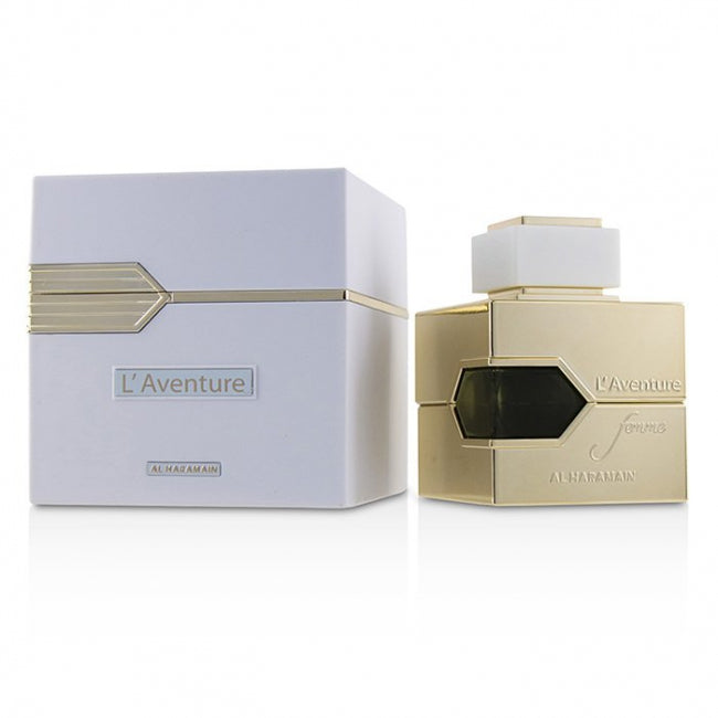 A photograph of L'Aventure Femme Eau De Parfum bottle and packaging. The bottle is gold with a white label and the packaging is white with gold accents.