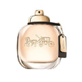 A glass bottle of Coach the Fragrance with a gold cap and a floral design, including an illustration of a horse and carriage.
