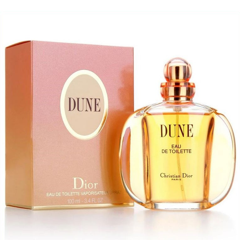 A photograph of Dune Eau de Toilette by Dior, showing a clear glass bottle with a golden cap, alongside its pink packaging box.