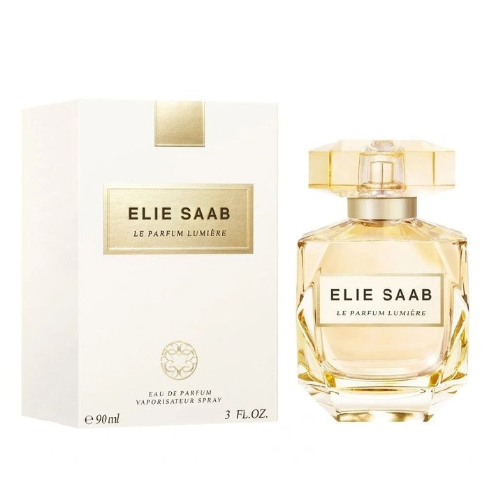 A product image featuring the packaging and bottle of Le Parfum Lumier by Elie Saab. The bottle is transparent, revealing a golden amber liquid, with a white cap and label.